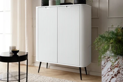 Biała komoda wysoka Luna z drzwiami i ryflowanymi frontami z czarnymi nogami