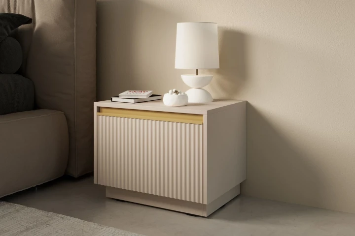 Beżowy stolik nocny Resto z szufladą i złotymi akcentami stojący